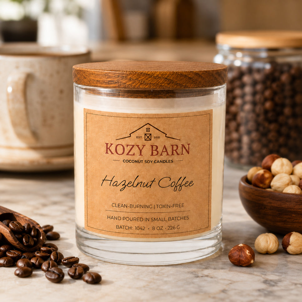 Kozy Barn candle with coconut soy wax and a wooden lid labeled Hazelnut Coffee styled on a marble surface with coffee beans, a bowl of hazelnuts, and a ceramic mug in the background.