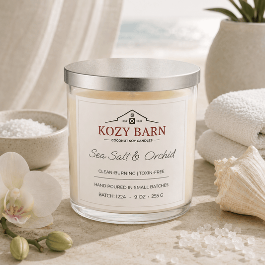 Kozy Barn candle labeled Sea Salt & Orchid sitting a beach table next too bowl of salt, orchid blossoms, sea shell and white spa towels.