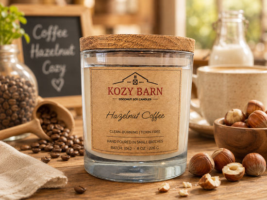 Kozy Barn candle labeled Hazelnut Coffee sitting on wood table next to coffee beans and cracked hazelnuts.