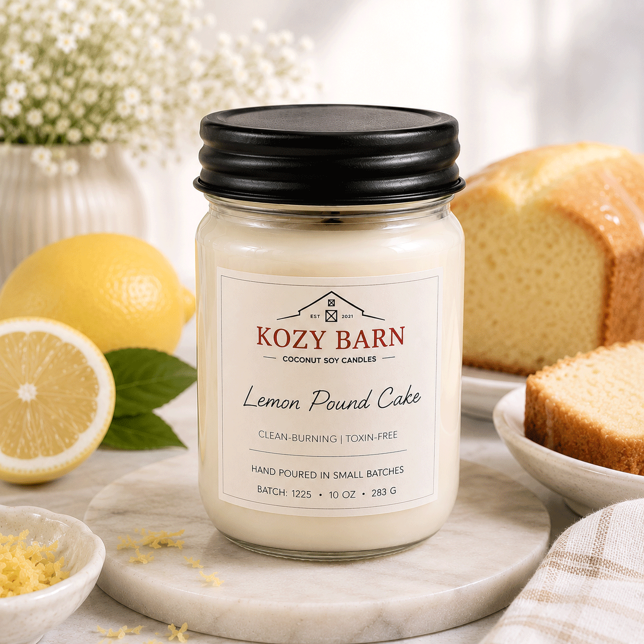 Kozy Barn candle labeled Lemon Pound Cake sitting next to freshly made lemon pound cake and sliced lemons. 