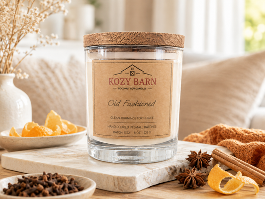 Kozy Barn candle labeled Old Fashioned sitting on table next to orange peel and spice.