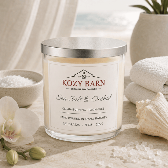 Kozy Barn candle labeled Sea Salt & Orchid sitting a beach table next too bowl of salt, orchid blossoms, sea shell and white spa towels. 