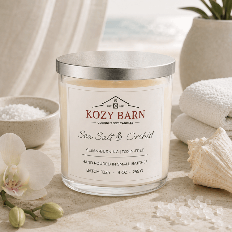 Kozy Barn candle labeled Sea Salt & Orchid sitting a beach table next too bowl of salt, orchid blossoms, sea shell and white spa towels. 